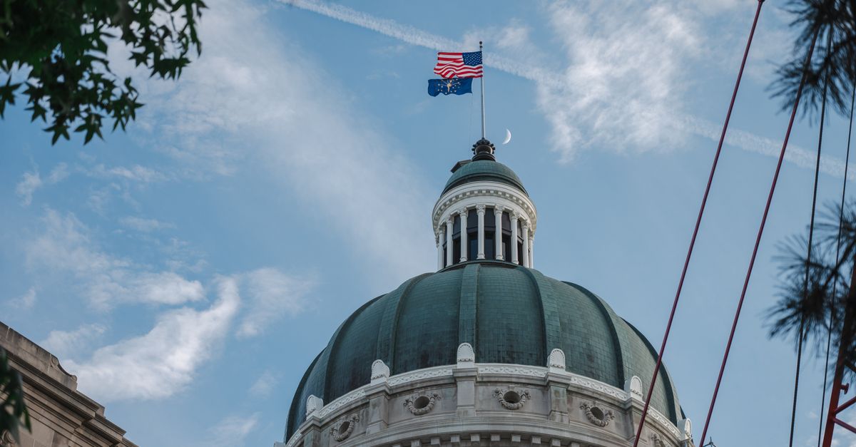 The Indiana State Capitol dome with American and Indiana flags flying against a bright blue sky.